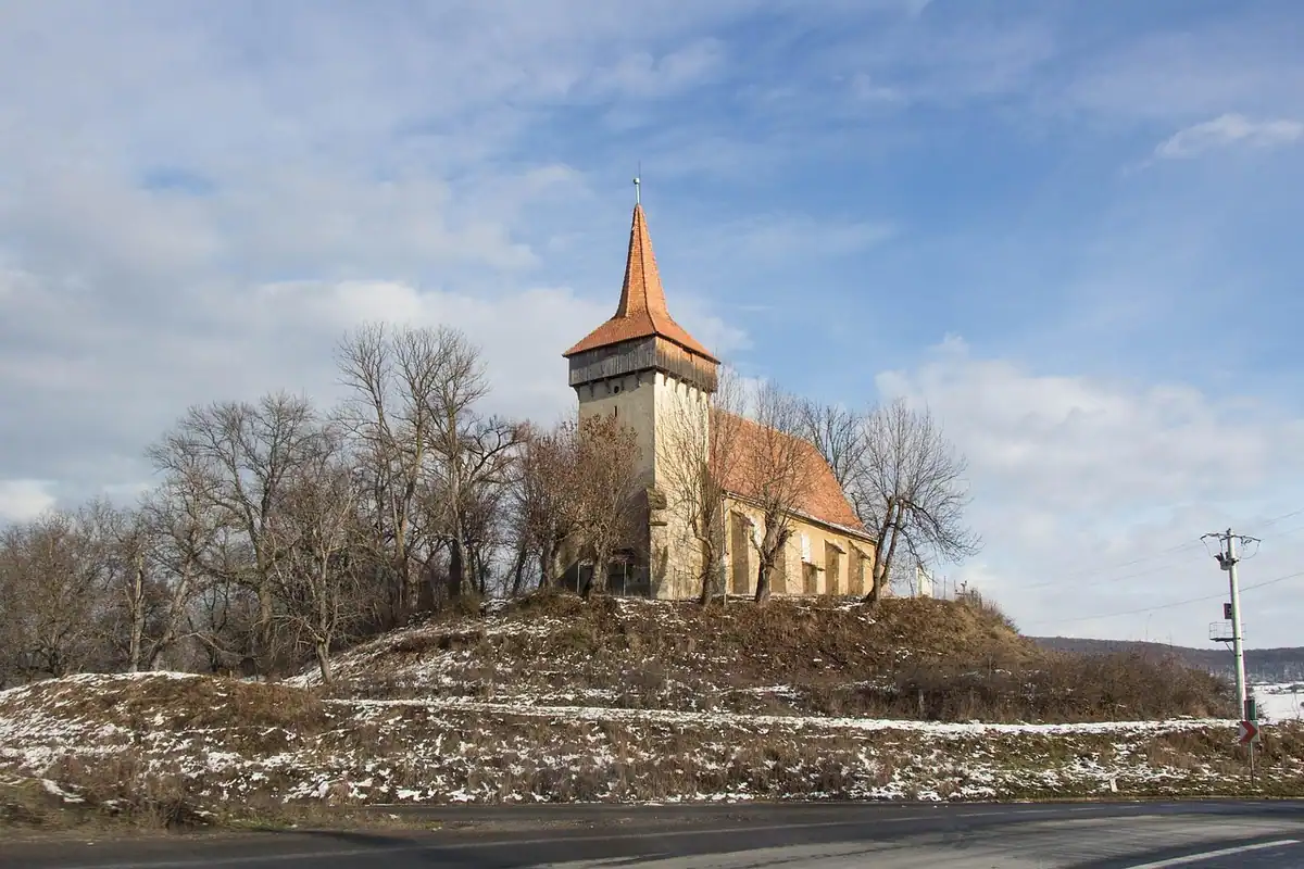 Biserică fortificată cu turn ascuțit, pe un deal din Transilvania, iarna