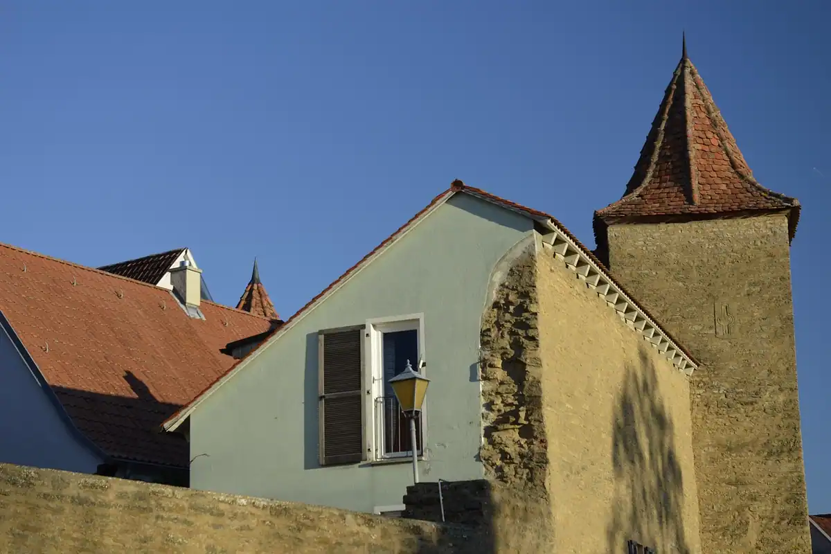 Zid de cetate și turn de piatră cu acoperiș ascuțit, într-un orășel medieval