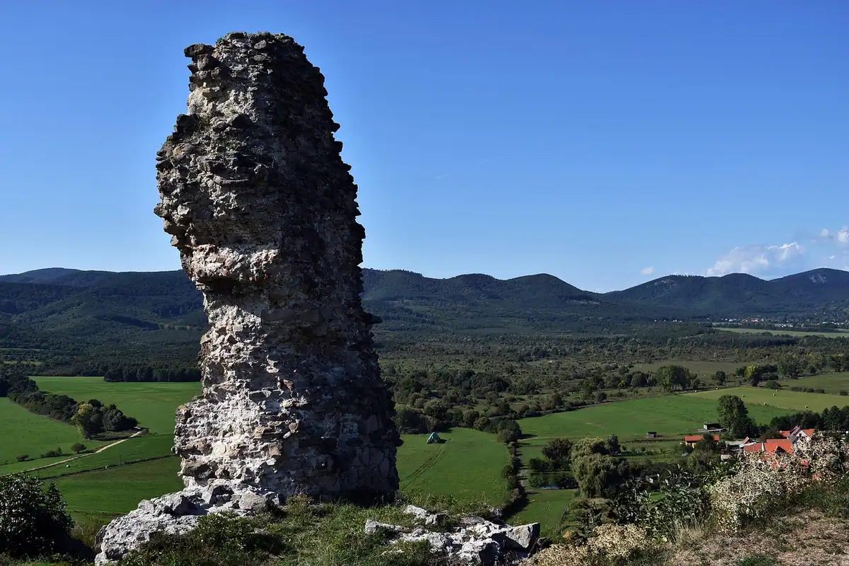 Ziduri și coloane de piatră rămase în pădure, pe un versant montan verde și liniștit