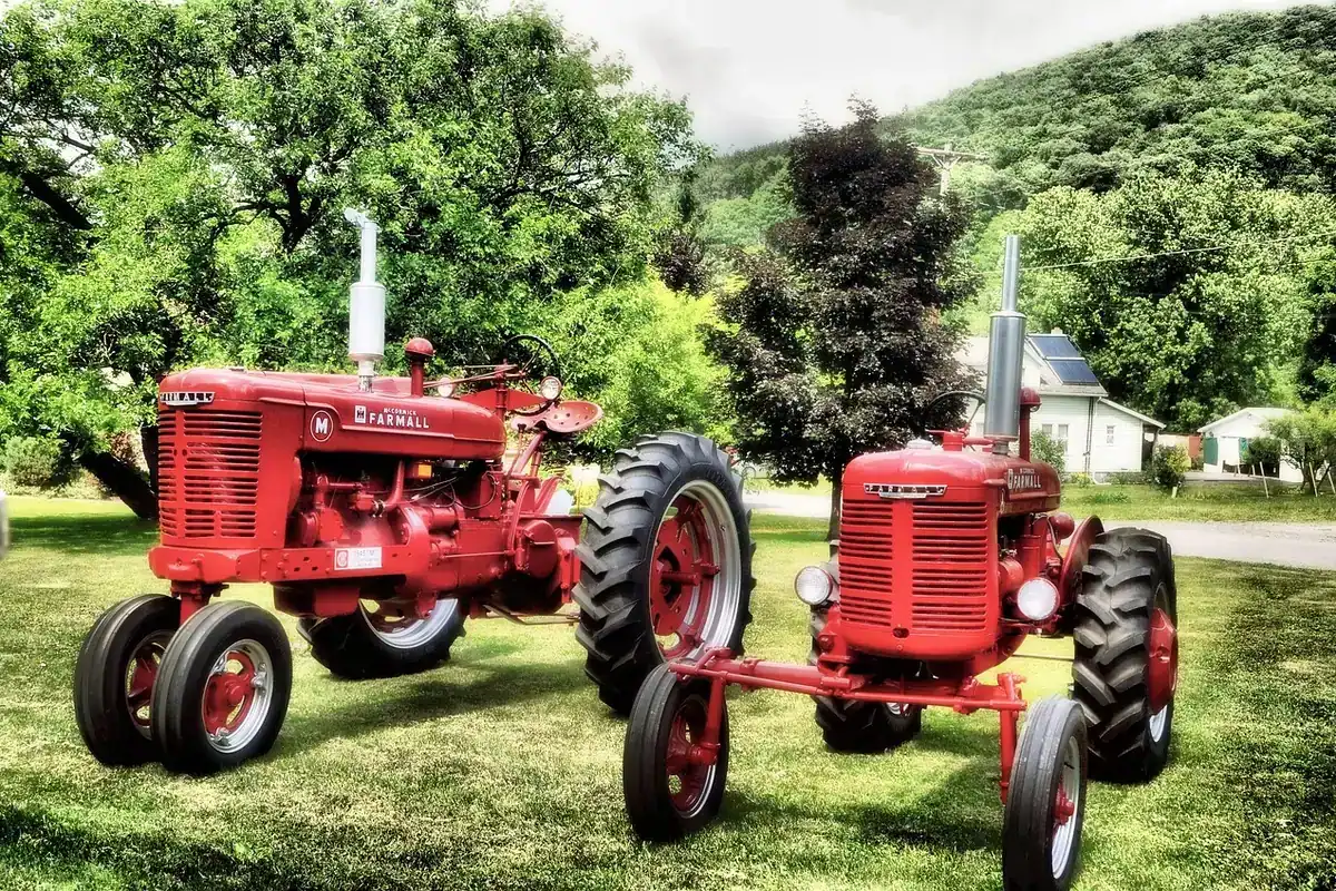 Tractor vechi, de culoare roșie, parcat pe un câmp verde într-o zonă rurală