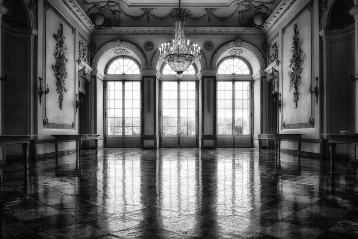 Sală somptuoasă de castel cu ferestre mari și decor baroc, văzută în alb-negru