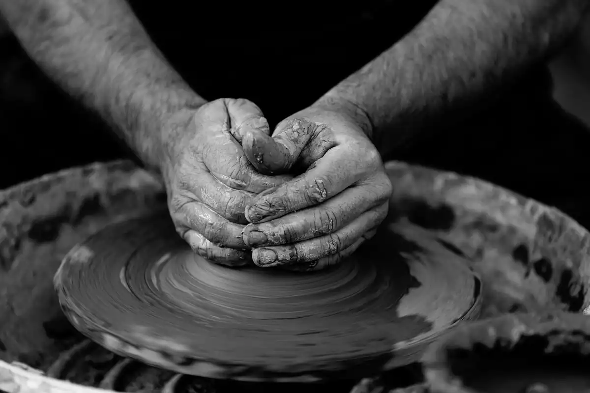 Mâini de meșter care modelează lut pe un vas ceramic, într-o fotografie alb-negru