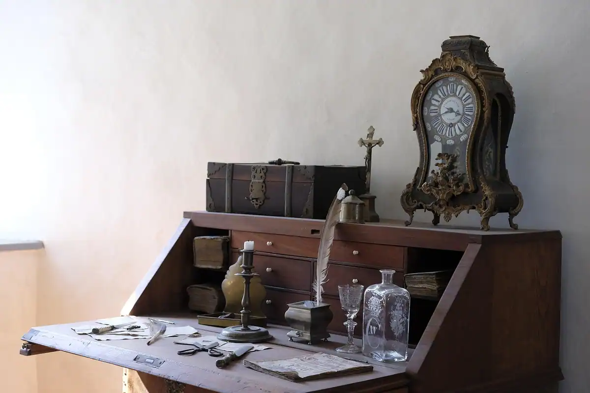 Ceas vechi cu pendul într-o carcasă înaltă de lemn, lângă un birou antic