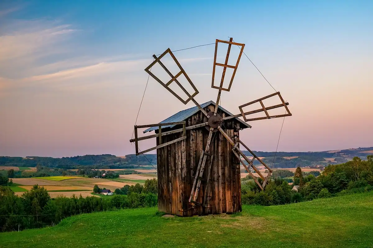 Moară de vânt din lemn pe un deal verde, într-un peisaj rural
