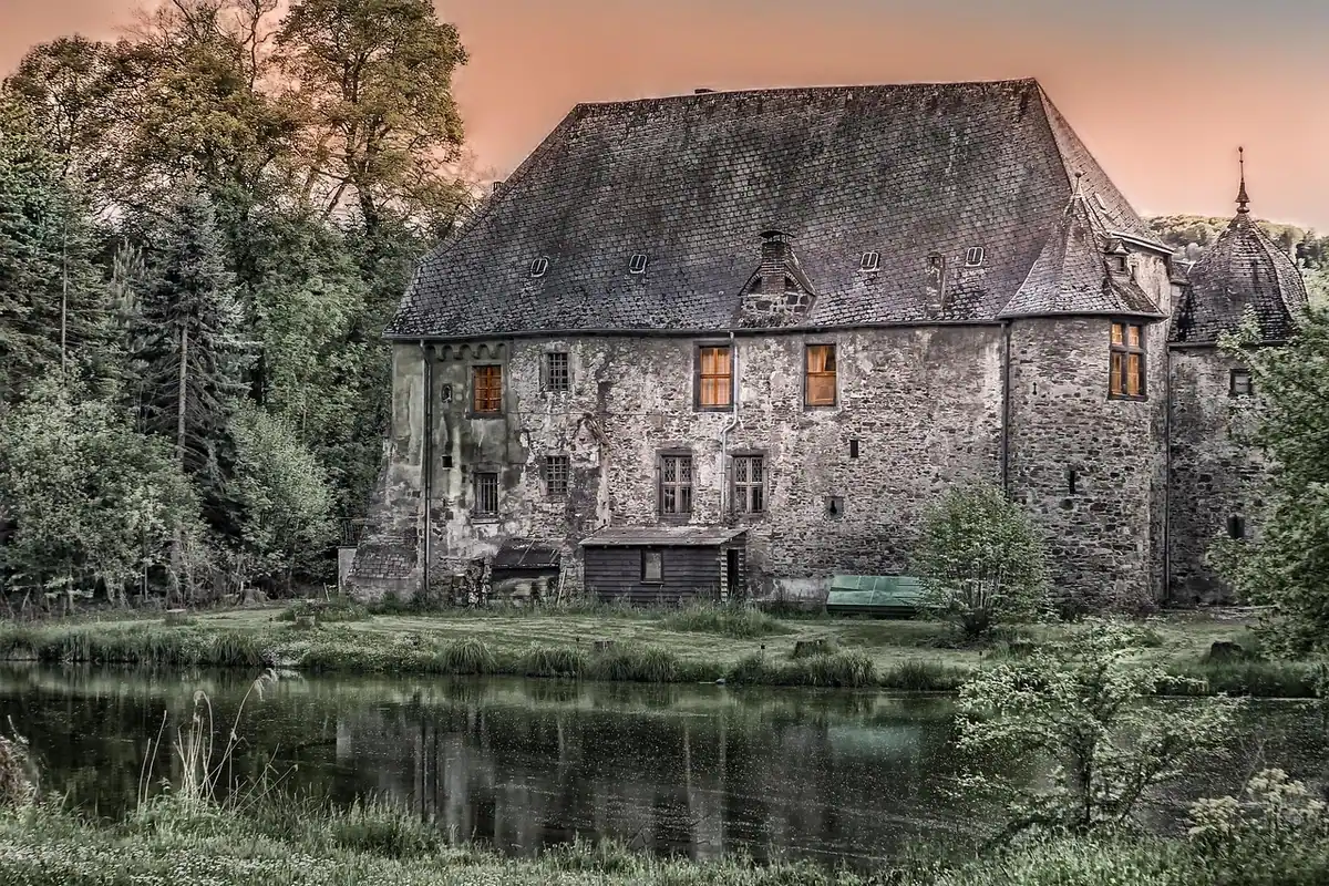 Casă veche de piatră cu acoperiș de ardezie, lângă un lac liniștit