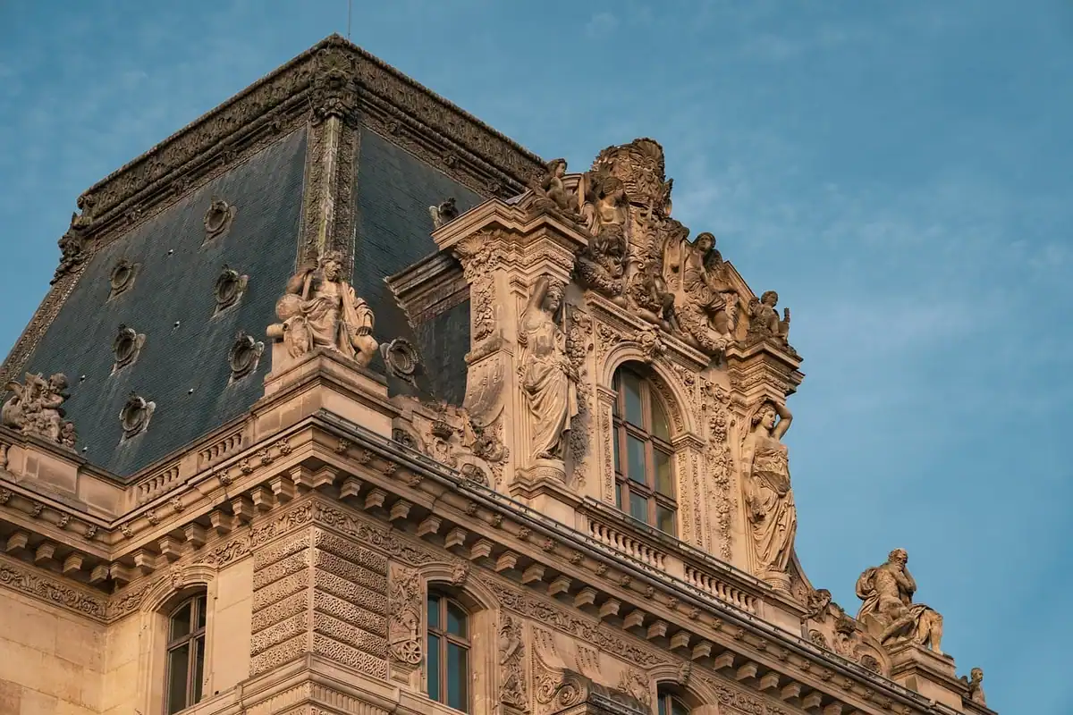 Fațadă sculptată din piatră a unei clădiri istorice, cu ferestre și acoperiș decorat