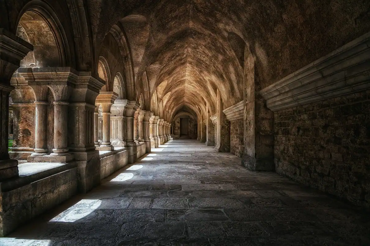 Galerie boltită cu arcade de piatră într-o mănăstire, străbătută de lumină