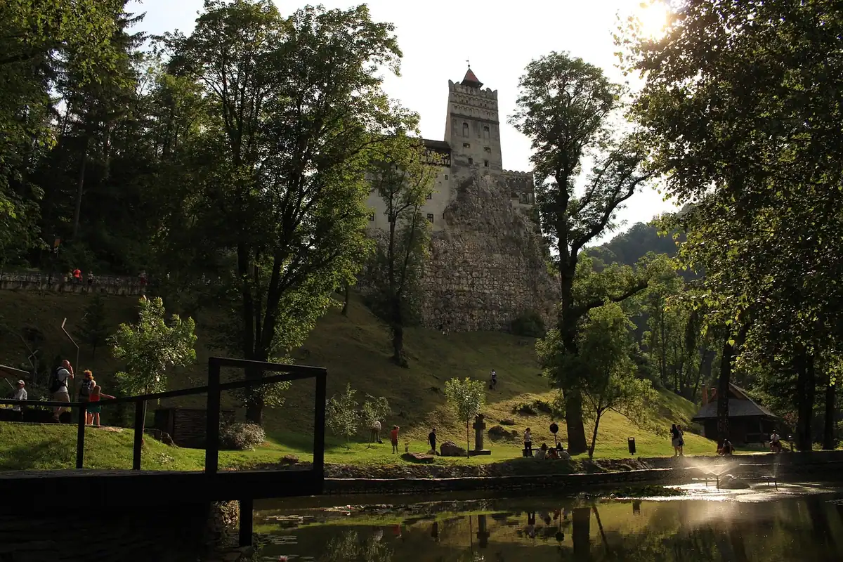 Castelul Bran printre copaci, văzut peste un lac liniștit