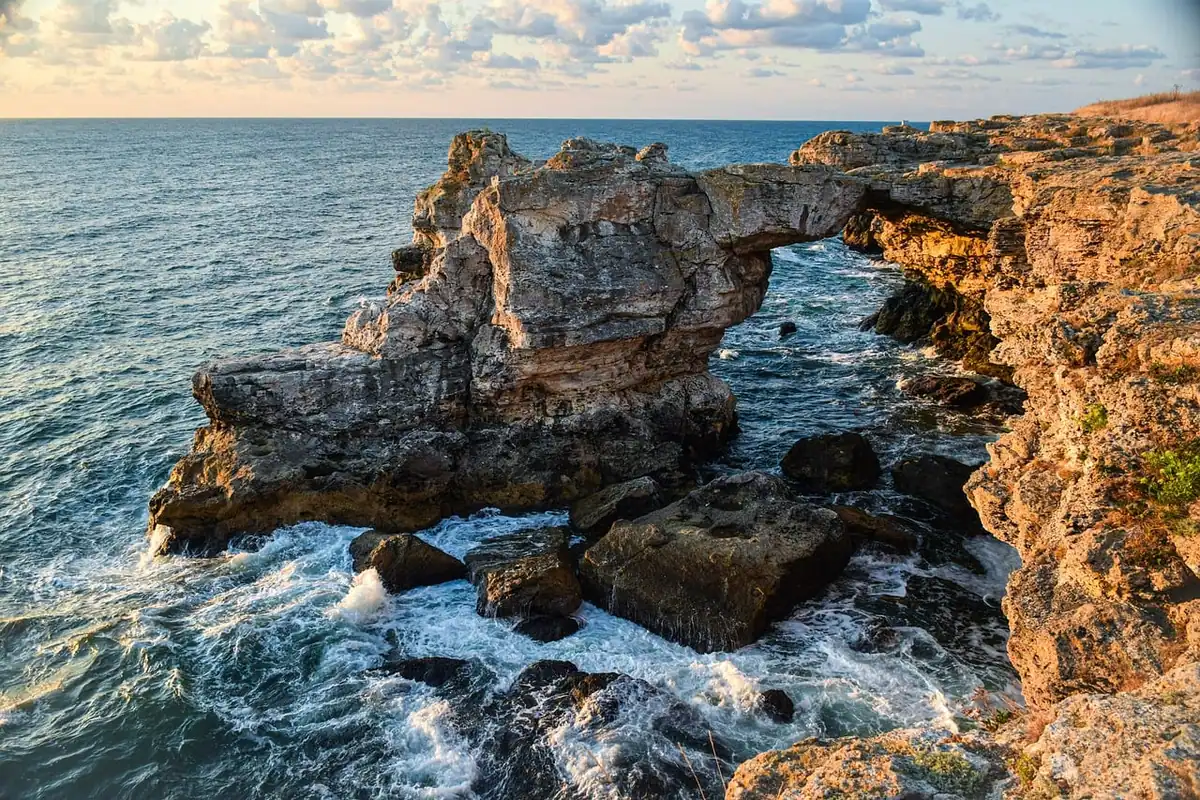 Stânci abrupte la mare, cu valuri și răsărit de soare peste apă