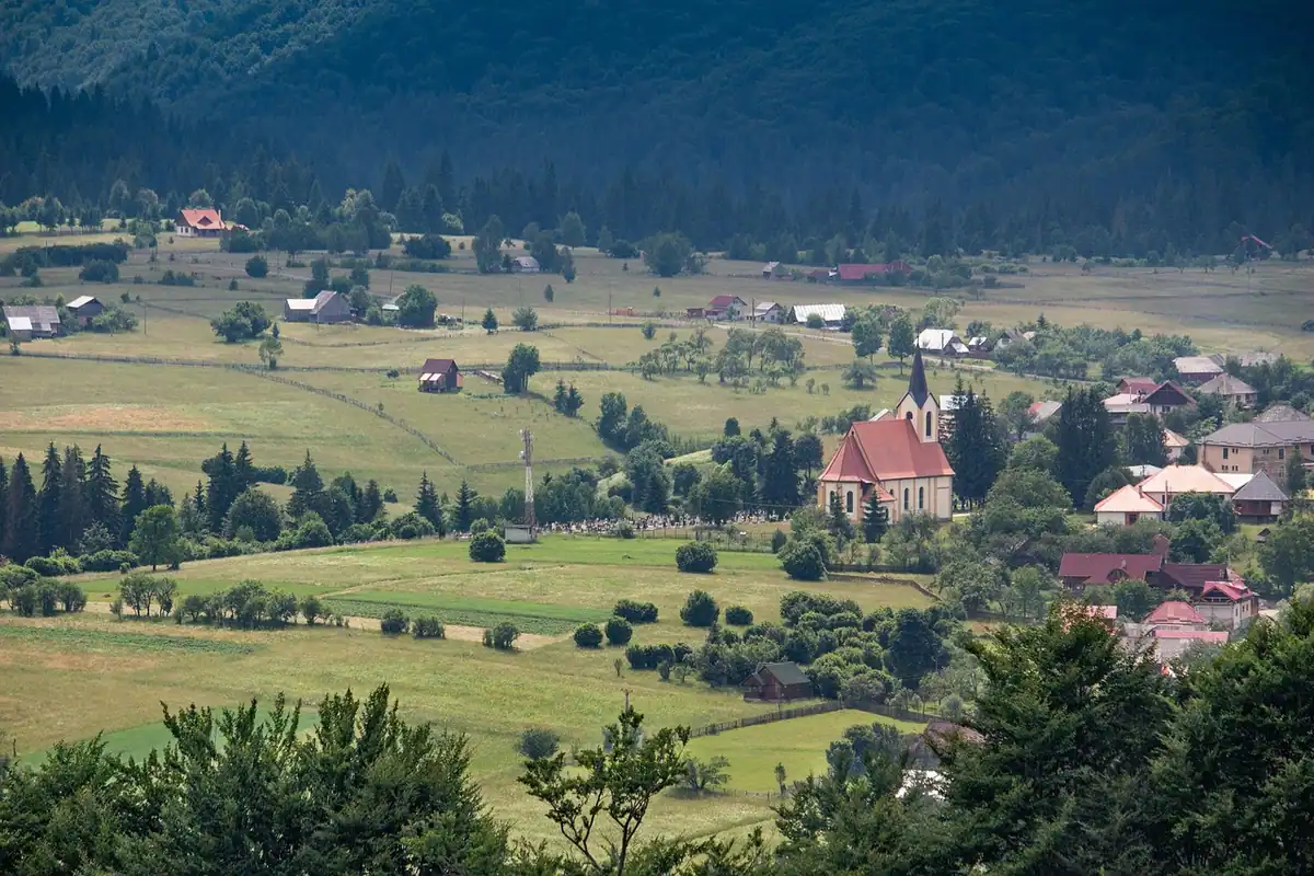 Sat cu biserică în fundul unei văi din Transilvania, cu păduri în jur