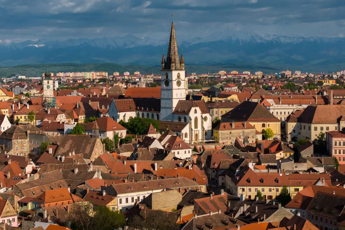 Orașul vechi Sibiu cu acoperișuri roșii și turnul bisericii, sub munți